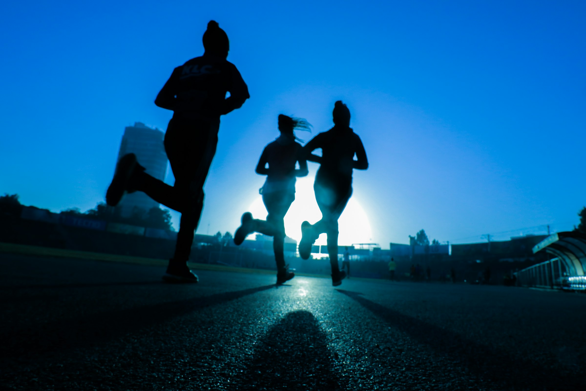 Trois coureurs en silhouette sur une piste, sous un ciel bleu
